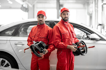 Portrait of two auto mechanics in red uniform standing with disks for wheel alignment at the car...