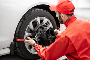 Handsome auto mechanic in red uniform fixing disk for wheel alignment at the car service