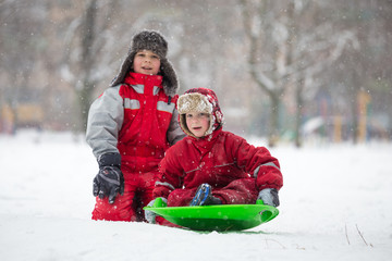 Two boys riding at the slide on snowy park