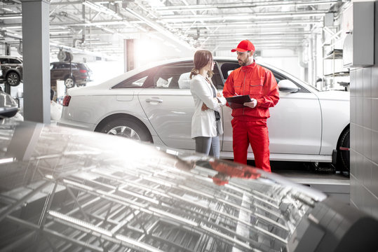 Young woman client with auto mechanic in red uniform at the car service. Wide angle view with copy space