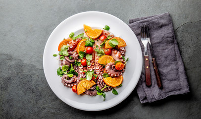 Whole octopus salad with orange, tomatoes and cress salad on white plate. Top view © lblinova