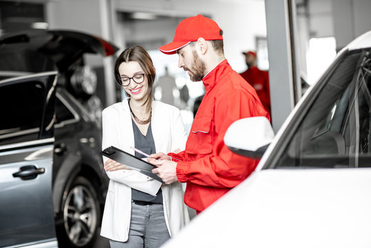Young woman client with auto mechanic in red uniform standing with some documents at the car service