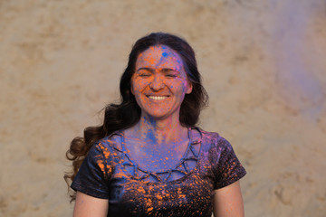 Closeup shot of lovely brunette model covered with colorful dry paint Holi at the desert