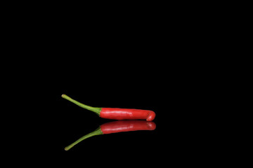 Small hot pod of red chili peppers on a black background with bright and clear reflection in the glass.