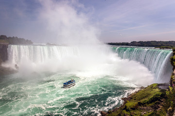 A touristic boat passing very close to a water fall in Niagara Falls in Canada in a blue sky day