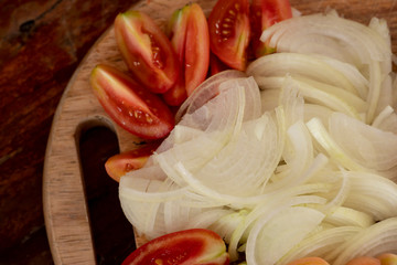 Sliced onion and tomato sliced on a wooden cutting board.