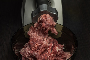 The cook grinds meat in minced meat on an electric meat grinder