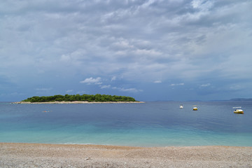 A green island in the azure sea. Beach, boats and cloudy sky. Primosten, Croatia,