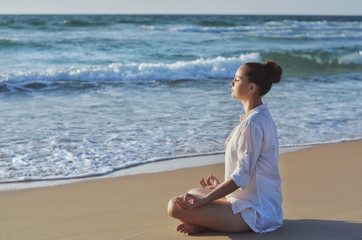 Young woman making meditation on the beach near the sea.