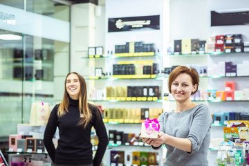 Positive smiling pleasant salesgirls suggesting perfume in modern cosmetic store. successful sellers.