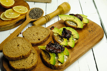Toasts with avocado and dried tomatoes on a wooden plate. Bread and chia seeds