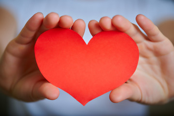 Obraz premium Valentine's Day theme with red paper heart in young woman's hands, close-up