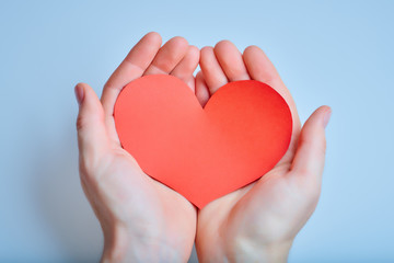 Hands with handmade red paper heart on the blue background