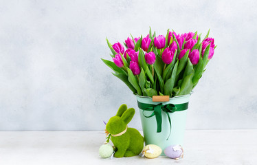 Violet fresh tulip flowers in pot with easter bunny on gray background with copy space