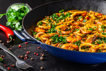 The concept of Spanish cuisine. Paella with seafood, shrimps, squid and greens, cooked in a wok pan on the street. street food.