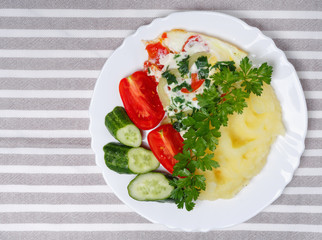 Hot tasty mashed potatoes with scrambled eggs, tomatoes, cucumbers and fresh parsley in  plate