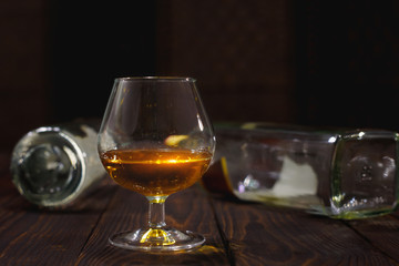 Glass of whiskey or brandy and empty bottles on wooden table