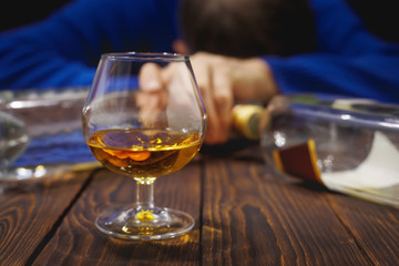 Male alcoholic with glass of whiskey and bottle sleeping on table at night.