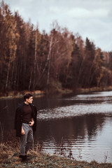 Fototapeta na wymiar A handsome young man standing near a lake in the autumn forest.