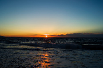 Naklejka premium The setting sun over the horizon at sea. Reflection of sunlight in the water. Small waves with foam.