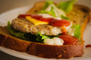 Hamburger made from whole wheat sliced bread, cheese, lettuce and topped with ketchup and slald dressing