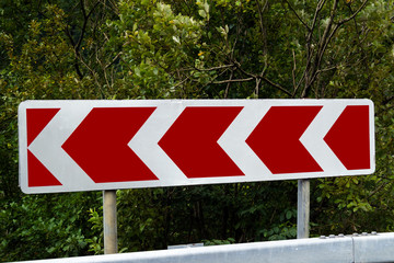 Road sign to the left. Red and white pointer. Direction of movement.