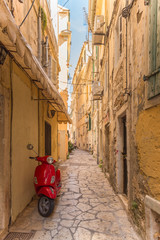Old narrow street, old buildings and red motorcycle on Corfu island, Greece.