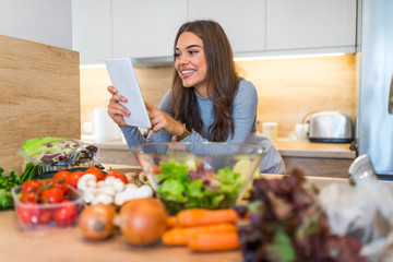 Smiling Young Woman Using Digital Tablet With Vegetable On Countertop In Kitchen