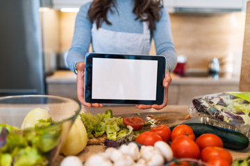 Young woman using a tablet computer to cook in her kitchen