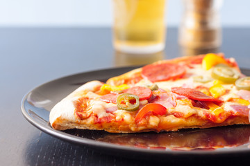 Low angle image of two slices of a pepperoni thin crust pizza with a glass of beer in the background