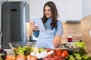 Young woman reading cookbook in the kitchen, looking for recipe