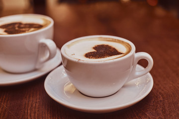 Two cups of hot coffee with art on the wooden table in a coffee shop, blur background with bokeh effect