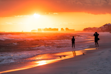 Fototapeta na wymiar Young couple looking at dramatic orange red sunset in Santa Rosa Beach, Florida with Pensacola coastline coast skyline in panhandle with ocean gulf mexico waves