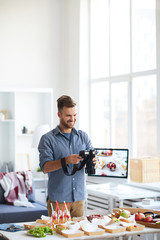 Waist up portrait of successful male photographer taking pictures of table with food while working...