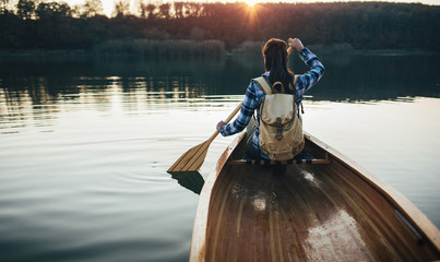Travel girl paddling the canoe on the sunset lake