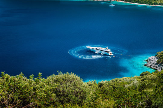 Luxury white yacht sail boat anchoring in a tranquil bay in deep blue water water, near picturesque shore of greek islands