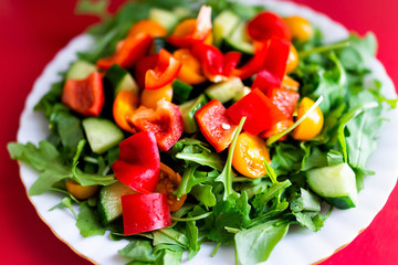 Closeup of fresh raw, chopped vegetable sald with arugula greens, red and orange bell peppers, tomatoes, cucumbers on table, colorful vibrant healthy lunch meal
