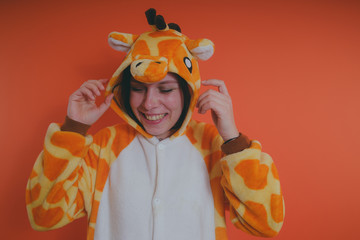 pajamas in the form of a giraffe. emotional portrait of a girl on an orange background. crazy and...