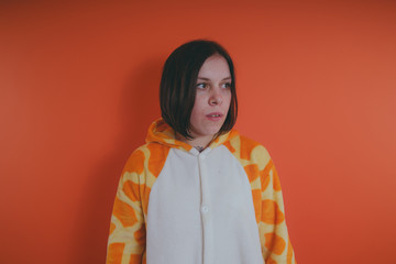 pajamas in the form of a giraffe. emotional portrait of a girl on an orange background. crazy and...