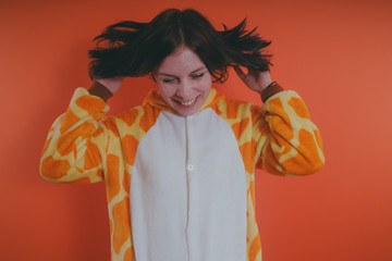 pajamas in the form of a giraffe. emotional portrait of a girl on an orange background. crazy and...