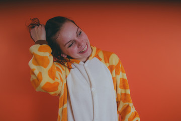 pajamas in the form of a giraffe. emotional portrait of a girl on an orange background. crazy and...