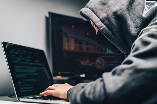 Cyber crime. Male hooded hacker with hidden face accessing to personal information on a computer in the dark. Technologal, cyber crime concept