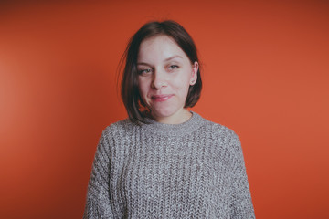 Young girl in warm grey sweater posing on orange background, woman with short haircut in knitted...