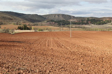 A brown earth plowed field in autumn with some farms on the background among the hills of Monterde rural town in Aragon region, Spain