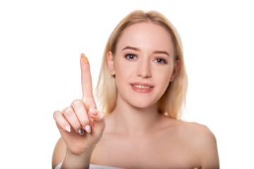 Focus on contact lens on finger of young woman. Young woman holding contact lens on finger in front of her face. Woman holding contact lens on white background.