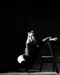 Young sexy blonde fashion woman sitting on floor in black body dress on dark night background