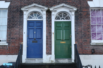 A blue and a green traditional English doors with white borders on a brick wall of a terrace house in Bristol, United Kingdom