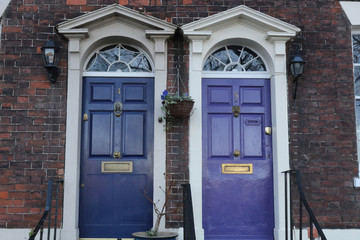 A blue and a violet traditional English doors with white borders on a brick wall of a terrace house in Bristol, United Kingdom