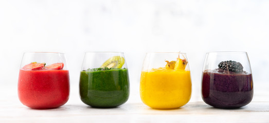 Four glasses with colorful detox smoothies on white background