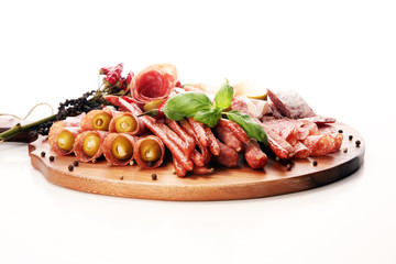 Food tray with delicious salami, pieces of sliced prosciutto crudo, sausage and basil. Meat platter with selection